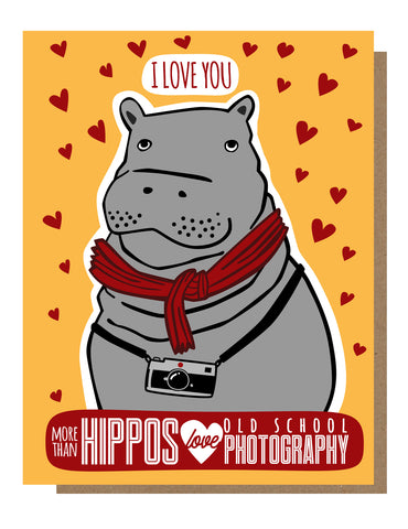 Greeting card featuring an illustration of a hippo wearing a scarf, with a background of heart shapes and the text 'I love you more than hippos love old school photography”